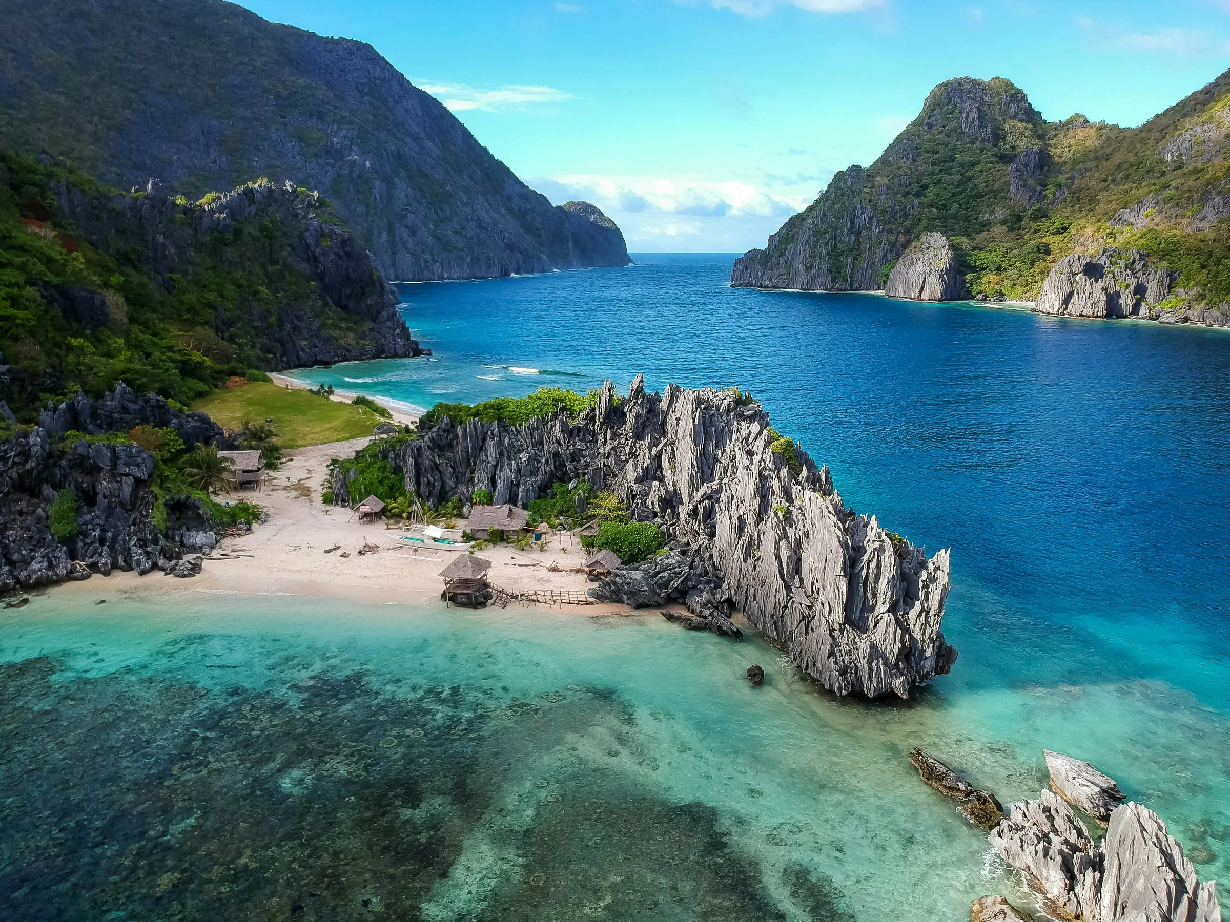 Aerial view of limestone cliffs framing a turquoise cove and secluded beach in the Philippines